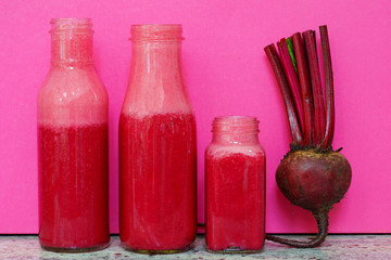Glass bottles filled with colorful fresh homemade beet smoothies on a pink background