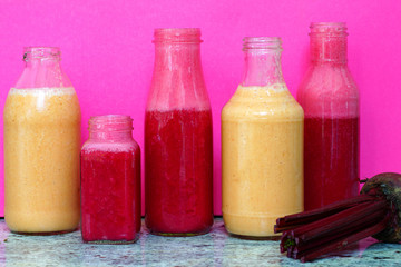 Glass bottles filled with colorful fresh homemade beet smoothies on a pink background