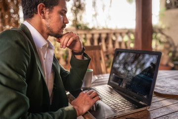  joven hombre de negocios con chaquete verde sentado en un jardin, trabaja desde casa con  un...