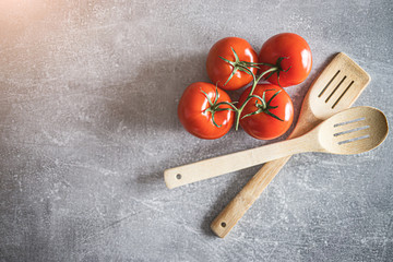Czerwone pomidory na gałązce obok drewnianych łyżek kuchennych.