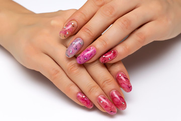 Multi-colored manicure on oval long nails with stains, abstraction with crystals close-up on a white background. Pink, fuction, purple, blue.