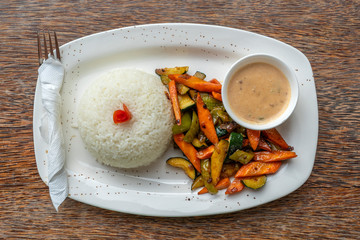 Fried vegetables, white rice and sauce on a white plate