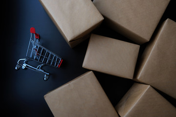 A small red shopping cart on black table with a lot of parcel or box brown paper wrapped. Concept of online shopping, Confirm sales or buy order by email, chat to provide product details. Work at home