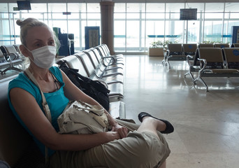 Woman in medical protective mask sits in an empty airport hall during a coronavirus pandemic.