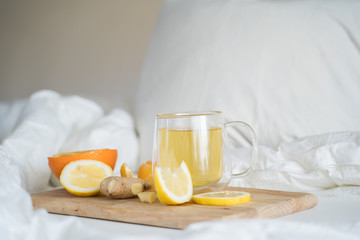 Cup with antipyretic drugs for colds,flu.Tea with citrus vitamin C,ginger root,lemon,orange.Wooden tray in patient's bed. Home self-treatment.Medical quarantine antiviral covid-19 coronavirus therapy