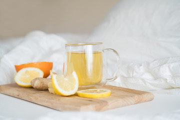 Cup with antipyretic drugs for colds,flu.Tea with citrus vitamin C,ginger root,lemon,orange.Wooden tray in patient's bed. Home self-treatment.Medical quarantine antiviral covid-19 coronavirus therapy