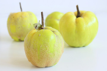 Ripe whole juicy quinces on white table in sunlight. Dark rustic style.Autumn fruits. Background for autumn. With a place for an inscription.
