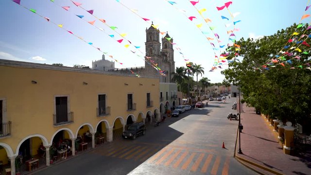 Wide angle panning right showing the cathedral San Gervasio and the Zocalo, or central park with flag waving in Valladolid, Yucatan, Mexico.