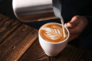 Barista pouring milk into cappuccino cup
