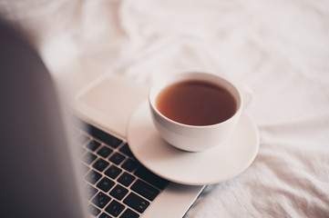 Cup of fresh black tea on open laptop in bed closeup. Working at home. Social distancing. Quarantine time.