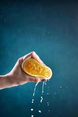 Hand squeezing the lemon on a blue background
