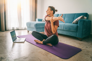 Aantrekkelijke jonge vrouw die yoga doet die yoga thuis online uitrekt. Zelfisolatie is heilzaam, amusement en educatie op internet. Gezond levensstijlconcept