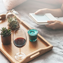 Woman reading electronic book with glass of wine on bed. Reading and relaxing during self isolation at home as preventative measure against virus outbreak. What to do during quarantine concept