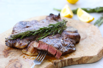 Marble beef grilled with lemon and rosemary on a wooden board on a light background. Slice of meat with a fork. Background image, copy space