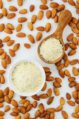 Almond flour in a bowl and spoon on a background of almonds. Vertical orientation, top view. Healthy food, gluten free.