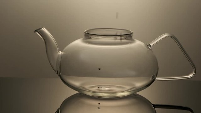 Black leaf tea drops in a glass teapot in slow motion