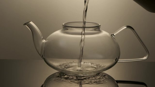 A stream of boiling water pours into a glass teapot in slow motion