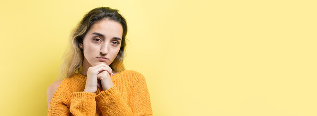 Portrait of a beautiful girl in an orange sweater, looks aside with pensive expression, is considering a plan for further action.