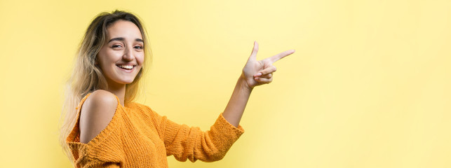 Happy young caucasian female in an orange sweater pointing fingers away