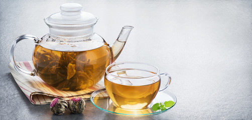 Bound tea in a transparent teapot and a cup of tea on a gray background.