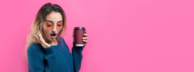 Obraz na płótnie Canvas Glamor woman in glasses in a blue sweater with a drink of coffee on a pink background