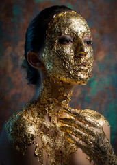 Girl with a mask on her face made of gold leaf. Gloomy studio portrait of a brunette on an abstract background.
