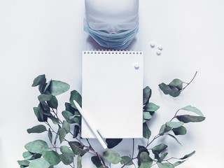 A skull in a medical mask is on a white background. Nearby are a branch of eucalyptus, notebook, pen, pills. The concept of protection against viruses, bacteria. Prevention of airborne diseases.