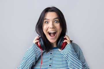 A young girl in a striped vest is listening to music in red headphones in a studio and dancing.