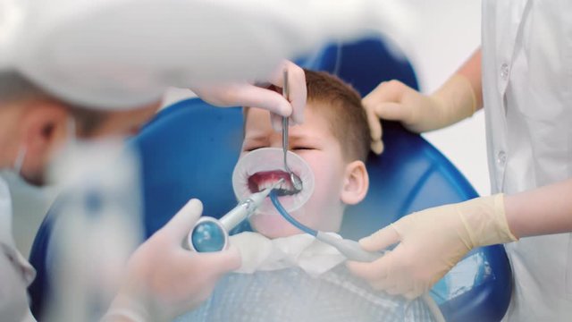 Boy sit in stomatology armchair surrounded by medical staff. Medium close up shot on 4k RED camera