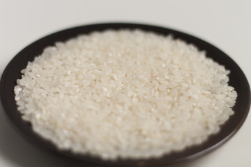 close-up of raw rice grits on a black plate on a light background. vegetarian food.