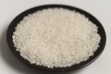 close-up of raw rice grits on a black plate on a light background. vegetarian food.