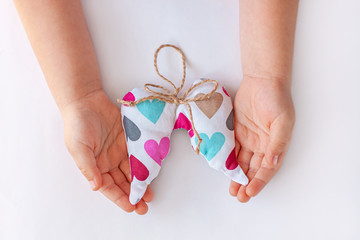 Children hands hold soft angel wings with colorful hearts and jute thread bow flat lay.Donation concept,Giving tuesday, handmade craft,love holidays Valentines Day.Minimalism creative style,copy space
