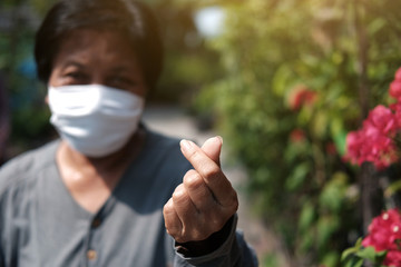 Asian old woman wearing white cloth mask for prevent the Covid-19 or Corona virus in Thailand and hand form mini Heart for protection of Air Pollution. Health of elderly concept. Closed up on fingers.