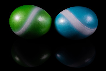 A green and a blue easter egg with a white stripe on a black reflective surface