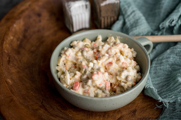 Bowl of traditional Russian salad called Olivie, Russian New Year or Christmas salad on wooden background. Salad from cooked vegetables. Potato salad.