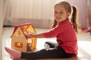 Indoor shot of baby girl playing with doll housewhile sitting at home during coronavirus...
