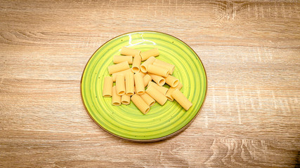 Uncooked raw rigatoni pasta on a green plate on wood background. Top view, selectiv focus, with copy space, space for text.