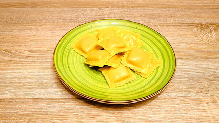 Uncooked raw ravioli pasta on a green plate on wood background. Top view, vertical photo, selectiv focus, with copy space, space for text.