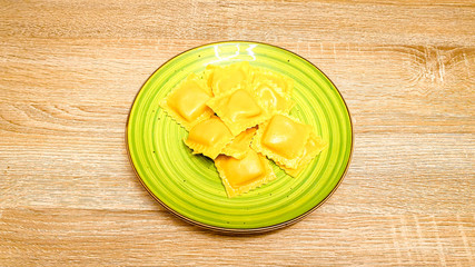 Uncooked raw ravioli pasta on a green plate on wood background. Top view, selectiv focus, with copy space, space for text.