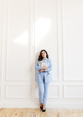 Fototapeta na wymiar Portrait of an attractive working girl freelancer businesswoman with black hair in a stylish blue suit against a white textured wall in the office at home