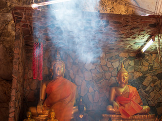 Fototapeta premium Buddha image statue inside cave with light smoke as travel peaceful place for relaxing holiday travel in Thailand destination.