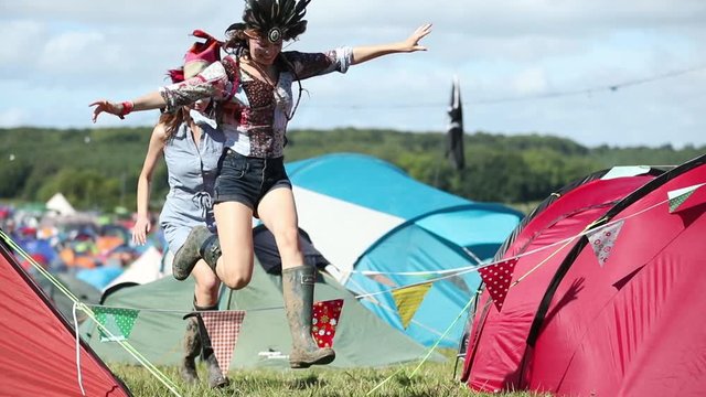 Friends jumping around on campsite between tents and having fun at summer festival