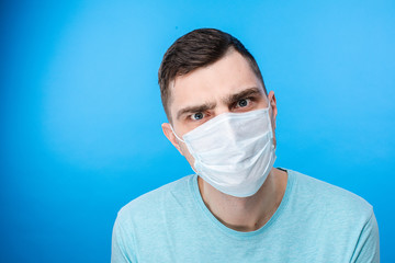 Waist up of handsome Caucasian man wearing blue t-shirt and mask protection from virus in studio. Infection and quarantine concept