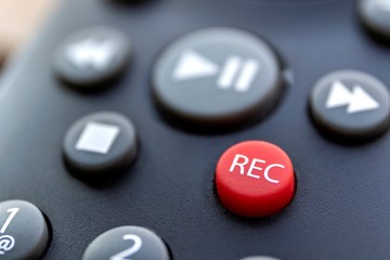 A close up portrait of the record button of a television or other multimedia device to start recording sound or a series or movie. it is surrounded by the buttons needed to play it again.