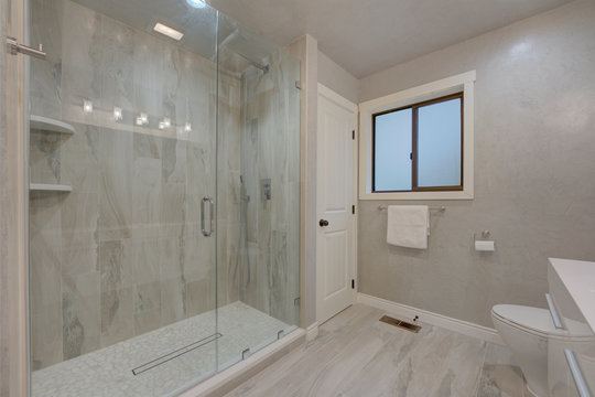 New modern bathroom interior grey venetian plaster, grey tiles, shower with glass walls, slick white shiny venity.
