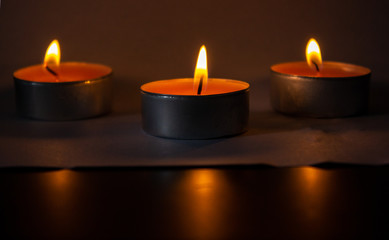 Composition of three candles on dark luxury night background. Black table, side view. Candles Burning at Night. Orange taper burning in focus, foreground. illustration design.