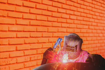 industrial worker welding process in factory close up with spark light and copy space on brick pattern background.