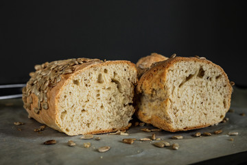 A homemade bread cut in half, covered in sunflower seeds, on baking paper, horizontal photo