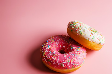 
Two juicy fresh sweet donuts with sugar icing and sprinkles on a pink background