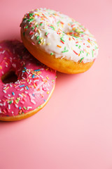 
Two juicy fresh sweet donuts with sugar icing and sprinkles on a pink background